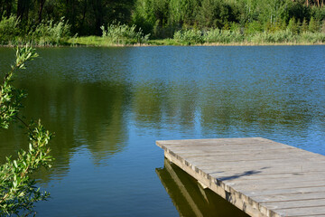 Obraz premium a wooden dock is in the water with a reflection of trees in the water 