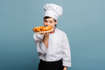 Young baker with down syndrome holding a plate of freshly baked croissants