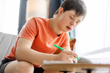 Young boy, teenager with down syndrome concentrating while drawing at home, closeup