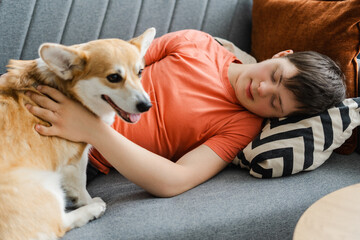 Teenager boy with down syndrome sleeping and hugging his corgi dog on sofa