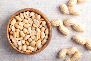 Roasted and salted peanuts in a wooden bowl on linen fabric. Ready-to-eat snack food, made from fruits of Arachis hypogaea, also known as groundnut, goober, pindar or monkey nut. Close-up from above.