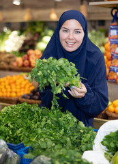 Girl in veil carefully chooses fresh parsley in a supermarket