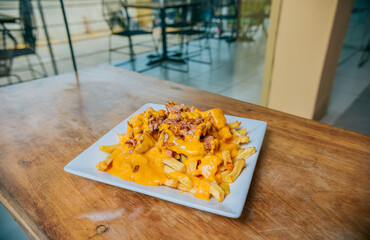 French fries dipped in yellow cheese with bacon on wooden table. Close up of french fries covered...