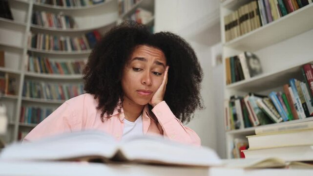 Boring curly student girl feeling tired during study at university library Stressed young woman exhausted from remote distance work or education hard program indoors
