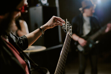 Medium closeup of unrecognizable bearded musician playing in rock band tuning electric guitar, copy...