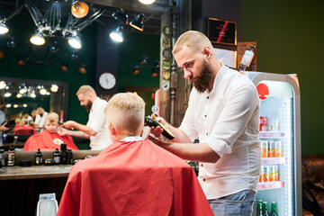 Barber using comb and shaver to cut hair. Professional hairdresser shaving little kid's nape.