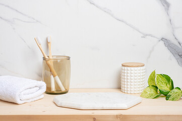 Marble pedestal for product montage with bamboo toothbrushes in glass holder, white towel and leaves on wooden table
