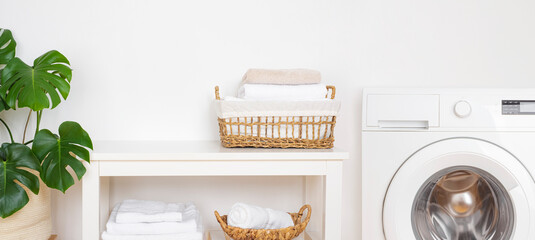 Light laundry room interior with washing machine, baskets and houseplant