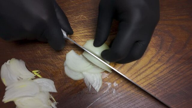 Man in black gloves cuts an onion on a wooden board