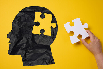 Silhouette of a human head holding a puzzle piece on a yellow background, representing mental health