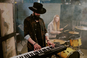 Bearded musician wearing stylish outfit with hat playing synthesizer in rock band, copy space