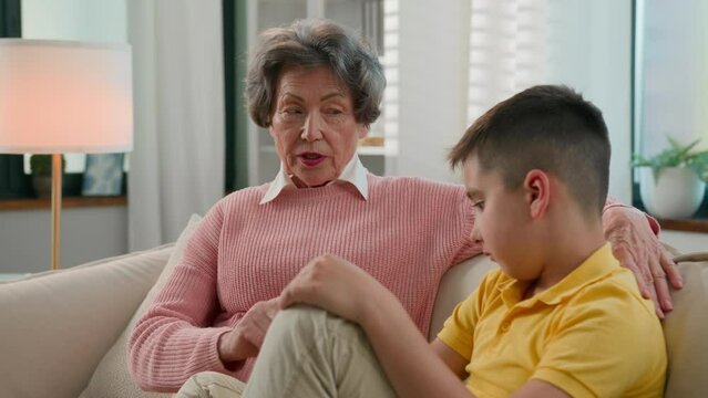 Caucasian family two generations strict serious old woman grandmother pensioner scolding offended grandson at home couch grandma punishing disobedient grandchild kid boy bad behavior demand discipline
