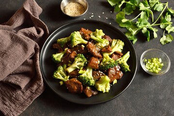 Beef with broccoli on black plate on dark stone background