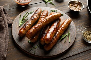 Grilled juicy thin sausages on wooden platter