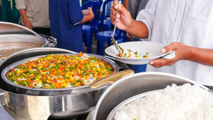 A buffet line with a variety of dishes including rice and vegetables Looks delicious, A person serves Rice and Vegetables at a Buffet table with multiple food warming containers.