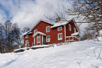 Naklejka premium Traditional old big red wooden house in winter countryside. Beautiful Swedish cottage or villa with big windows, terrace and balcony. Christmas landscape in northern Europe. Snowy village