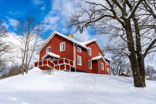 Traditional old big red wooden house in winter countryside. Beautiful Swedish cottage or villa with big windows, terrace and balcony. Christmas landscape in northern Europe. Snowy village