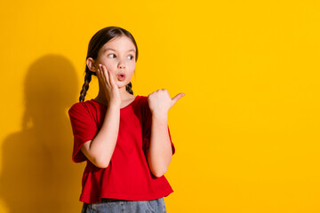 Fototapeta premium Photo of lovely small girl direct finger empty space wear t-shirt isolated on yellow color background