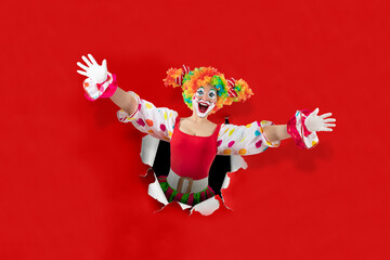 Funny female clown with open arms  looking through the ripped paper hole, woman entertainer as...