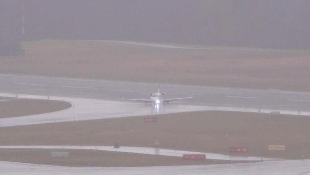 Business jet small light vacating turning of the runway onto taxiway at generic airport rain poor visibility bad weather conditions