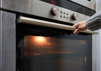 Hand of an unrecognizable person holds the handle to open the door of the oven where food is being baked