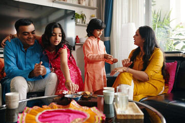 Indian family of four drinking tea together at table in the room