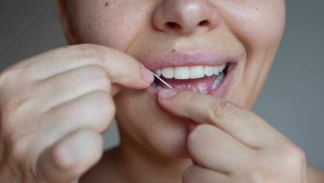 Close up of a young caucasian woman flossing her teeth on a dark gray background. Oral hygiene, dental health care, morning and evening routine. Close-up. Dentistry concept