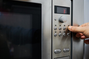 Hand of an unrecognizable person operating the microwave, pressing the button to select the...