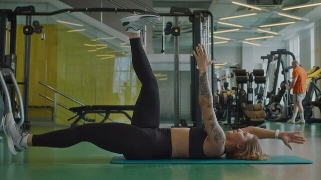 Side-view shot of young slim woman lying on yoga mat at gym doing dead bug exercise during core workout