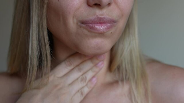 Sore throat. Young caucasian blonde woman with a throat pain holding her neck with hand on a grey background. Flu, cold, nausea, tonsillitis, sars virus, inflamed tonsils. The pill got stuck in throat