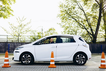 Woman sits in car , driving back and looking at the cones set up close to car