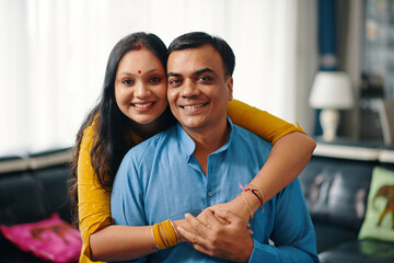 Portrait of lovely Indian couple embracing and smiling at camera while spending time at home