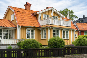 Old wooden yellow house with big balcony. Typical Swedish house surrounded by palisade fence. Beautiful wooden fence of natural wood is not painted. Ecological design.