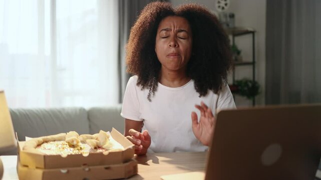 Portrait of young curly woman eating pizza fast food and having toothache sitting at desk at home workplace Sad female feeling pain in tooth because caries gum disease or sensitive teeth indoors