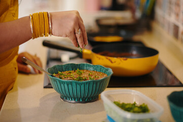 Close-up of housewife adding greens in dish while cooking in the kitchen