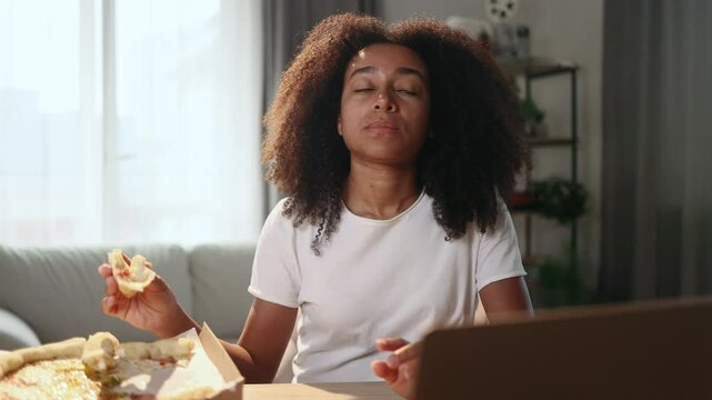 Portrait of young curly woman eating pizza fast food and having toothache sitting at desk at home workplace Sad female feeling pain in tooth because caries gum disease or sensitive teeth indoors
