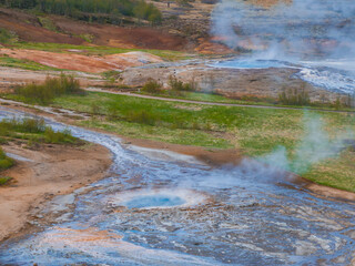 A stunning aerial view of a geothermal area in Iceland, featuring a steaming hot spring with a blue...