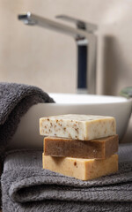 Handmade beige soap bars on dark grey towels, near plant and basin in bathroom, mockup