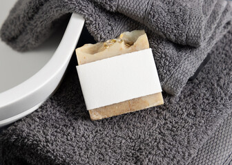 Soap bar with blank label on dark grey towels near vessel sink in bathroom closeup, mockup