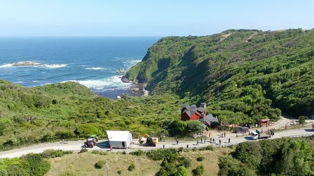 Aerial View Of Tractor Pulling House Across Road In Chiloe, Chile. This Is called Minga, A South America term meaning - coming together for the common good. Pull Back Ascending Shot