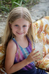 Fototapeta premium Cute little girl holding a glass full of fresh made lemonade, summer refreshing drink, healthy lifestyle concept, hydration and healthy diet during hot summer days.
