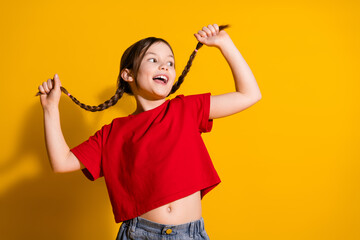 Photo of lovely small girl pull hair empty space wear t-shirt isolated on yellow color background
