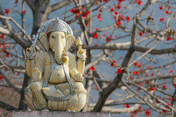 God Ganesha against the background of a tree blooming with red flowers.