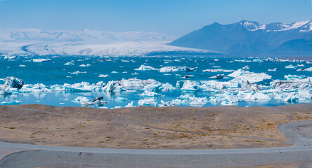 Stunning aerial view of a glacial lagoon in Iceland, featuring floating icebergs on turquoise water and snow-covered mountains in the background.