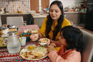 Mother Feeding Her Son At Table During Dinner