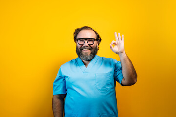 Doctor in blue coat on yellow background gesturing, with OK expression.