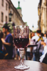 Elegant wine glass on rustic table amidst bustling city life, showcasing relaxed urban indulgence.