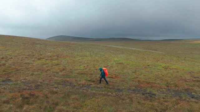 Aerial side view of tourist carrying orange backpack and exploring towards Five Stones on a cloudy day in EngLAND.