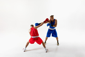 Two athletes dressed red and blue uniform, in heat of battle, each focused on improving their combat skills against white studio background. Concept of professional sport, competition. Ad