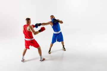 Two skilled fighters, boxers in blue and red attire, in high-energy sparring match to enhance their abilities against white studio background. Concept of professional sport, competition. Ad